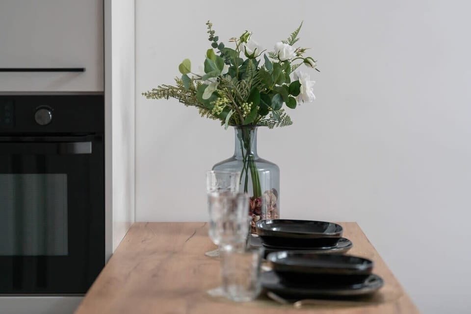 A wooden dining table set elegantly with glassware and greenery, offering a chic dining experience.


