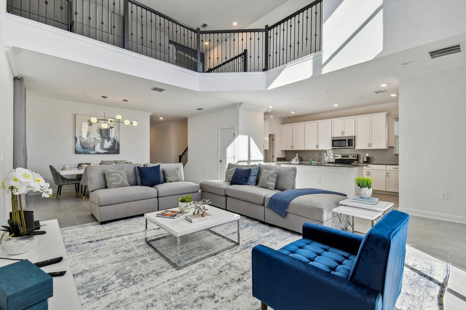 Enjoy a stylish and comfortable living area with soft gray sofas and vibrant blue accents. High ceilings and ample natural light create an inviting atmosphere, ideal for relaxation or social gatherings with friends and family.