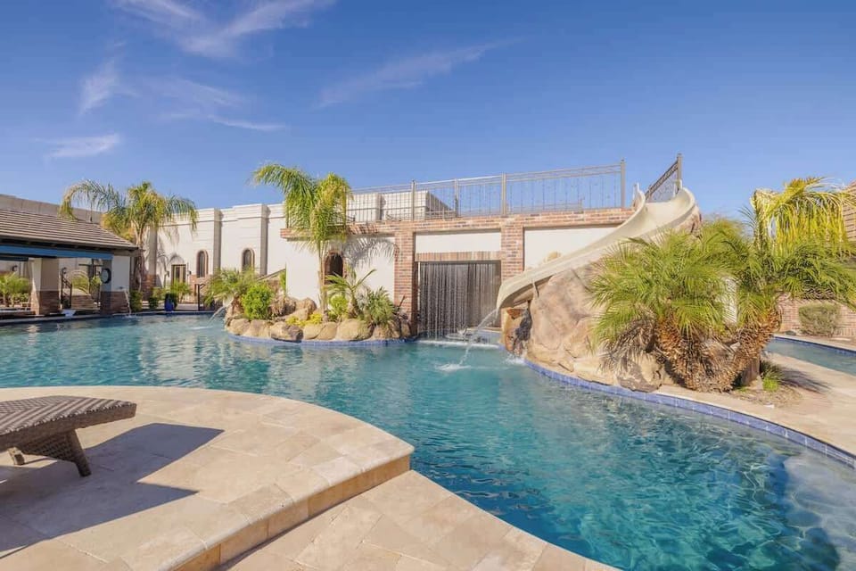 Slide into Fun! – Expansive resort-style pool with dual waterslides, waterfall feature, and palm-lined landscaping.