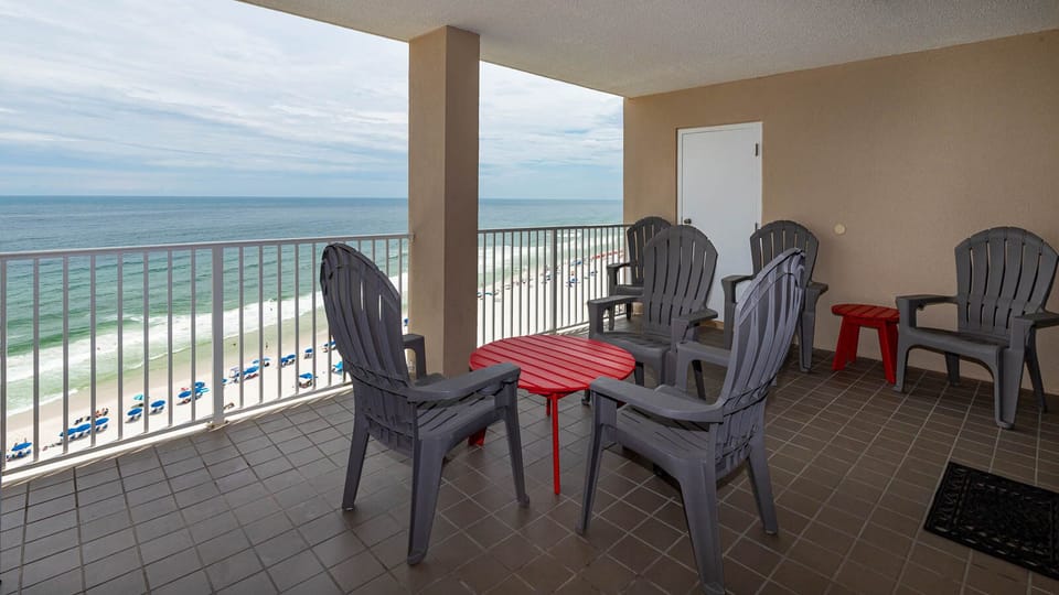 Relax on the balcony with gray chairs and a red table, enjoying the stunning beachfront view