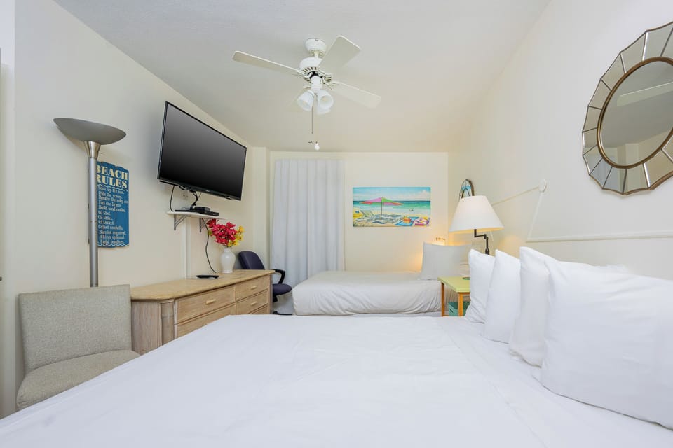This cozy bedroom features two comfortable beds, a mounted TV, and cheerful beach-themed decor for a relaxing stay