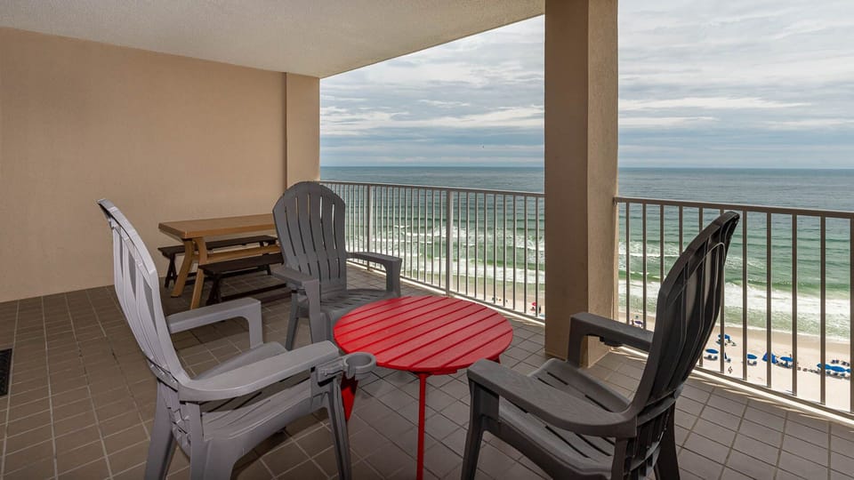 Enjoy a beachfront view from this balcony featuring comfortable seating and a vibrant red table for relaxation