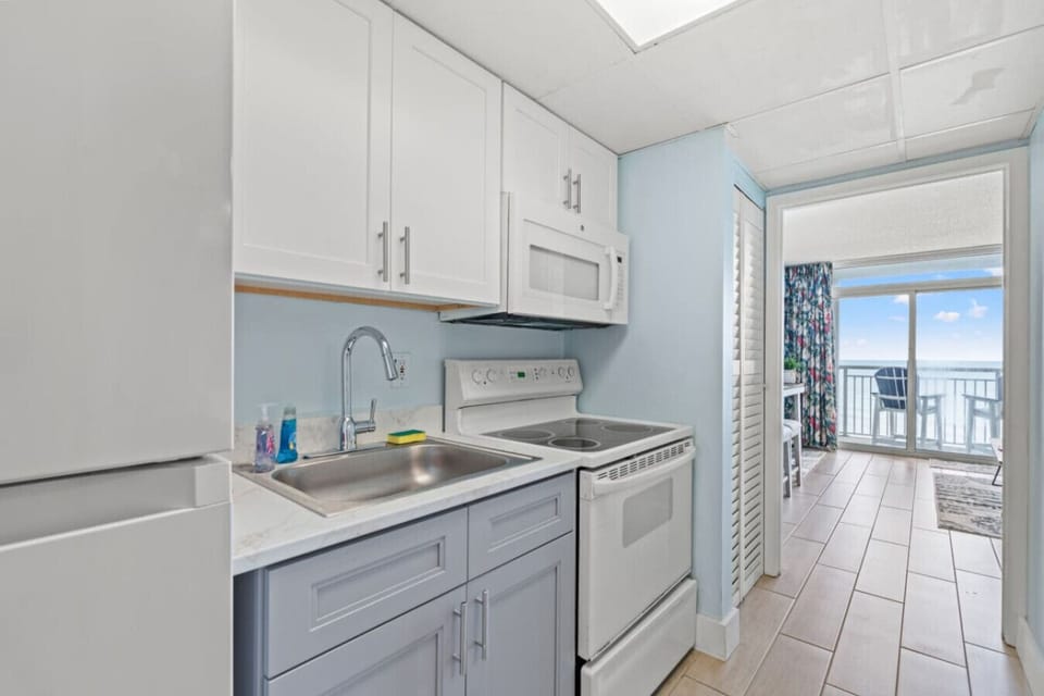 Remodeled kitchen with white and gray shaker cabinets, full-size refrigerator, microwave, stove, and oven. Fully stocked with dishware, silverware, cookware, and a full kitchen sink for convenient meal preparation during your stay.