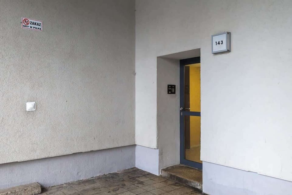 Exterior entrance of the building with a neutral facade and yellow door, giving a glimpse into the quiet residential setting.

