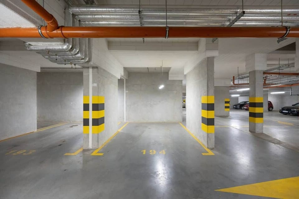 An underground parking area with clearly marked parking spaces, yellow and black safety columns, and bright lighting.
