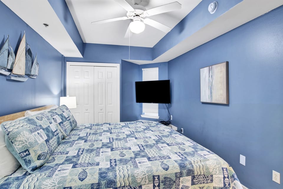 Master bedroom with king bed, 2 nightstands, wall mounted smart TV, double coset, ceiling fan and an ensuite bathroom