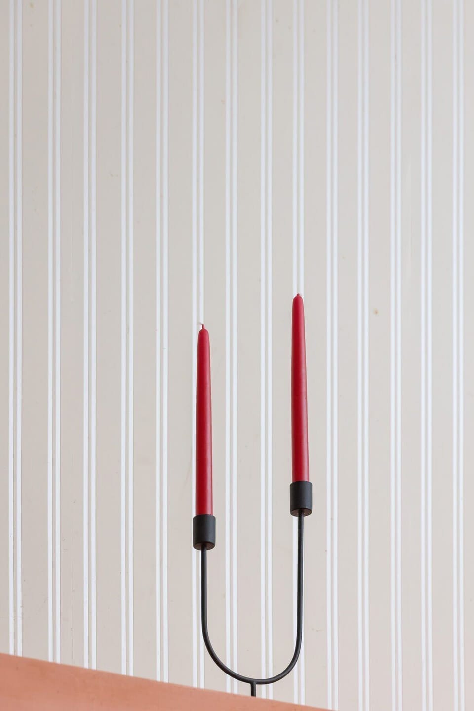 A minimalist wall decoration with two red candles on sleek black holders, contrasting against a light backdrop.

