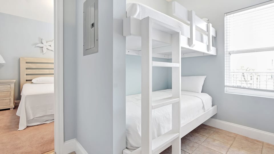 Compact bedroom featuring a white bunk bed with natural light from a nearby window