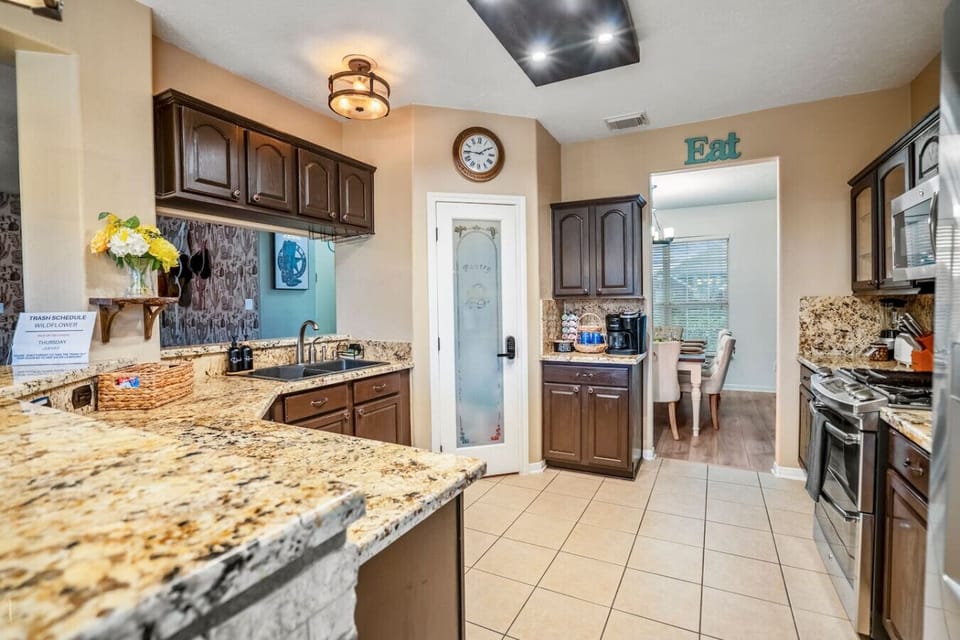 Granite kitchen with dark cabinets, coffee station, and frosted glass pantry door