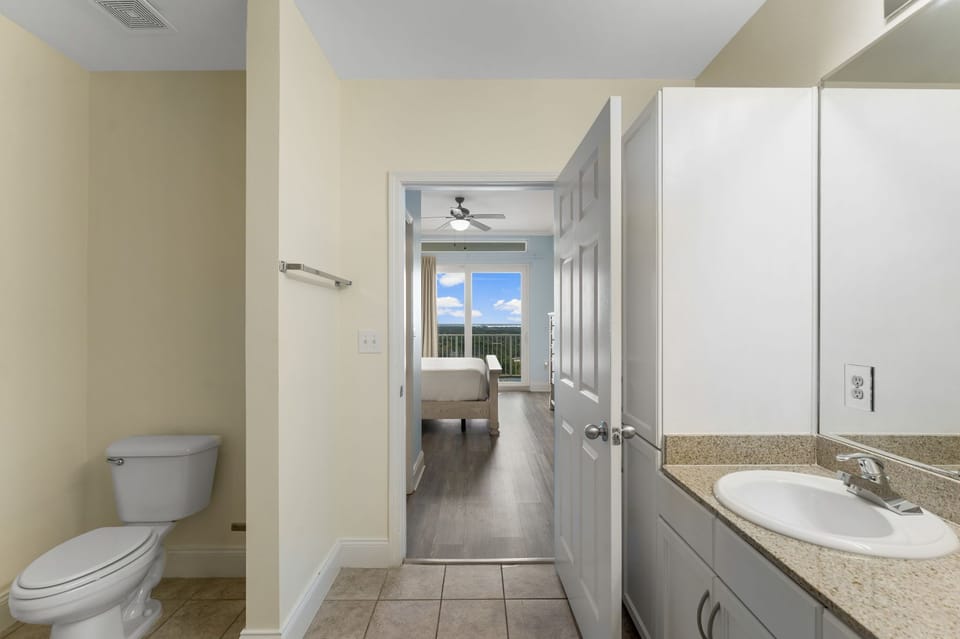 View from the bathroom into a bedroom with a balcony overlooking the ocean.