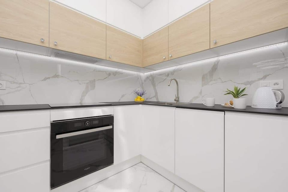 A modern white kitchen with wooden accents, a built-in oven, and a marble backsplash, combining aesthetics with functionality.

