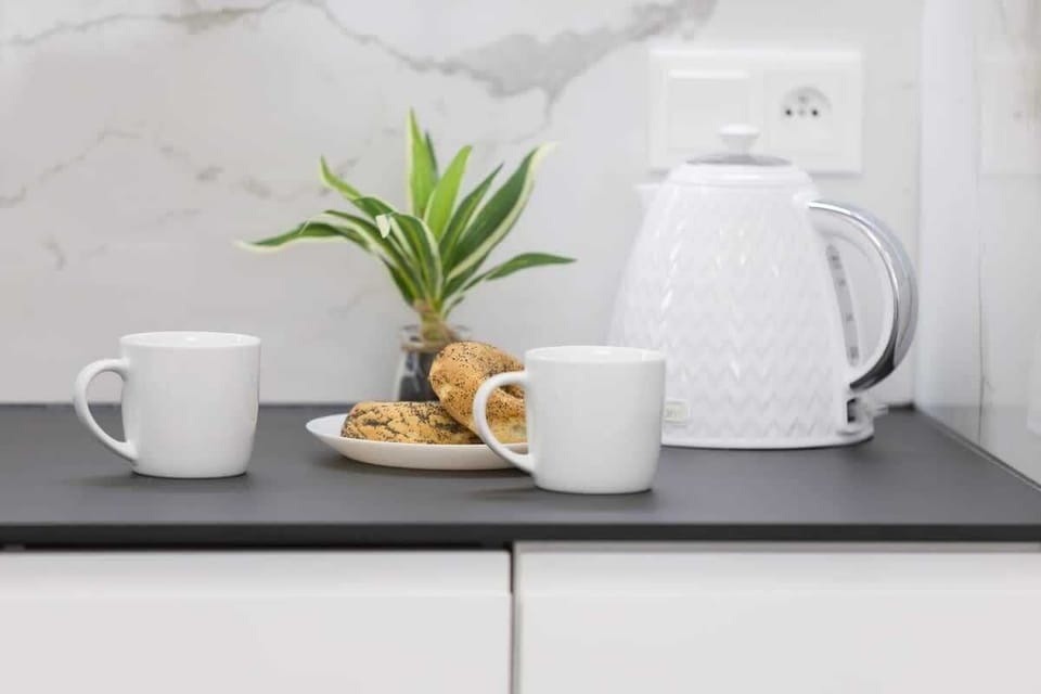 A cozy breakfast setup with a white teapot, two cups, a potted plant, and a croissant, creating a warm and inviting morning atmosphere.



