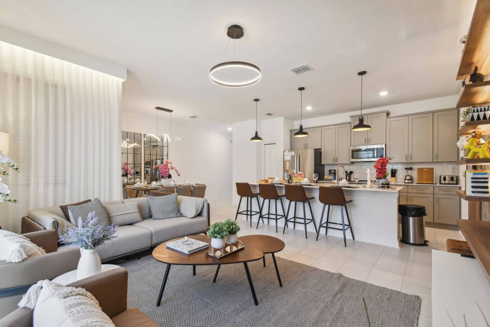 Experience a bright, modern living space with sleek cabinetry and warm wood accents. The cozy seating area features a plush gray sofa and stylish coffee table, flowing effortlessly into a chic kitchen—ideal for socializing.