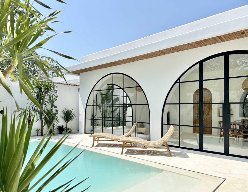 A swimming pool with daybeds, an outdoor shower, and a lush garden