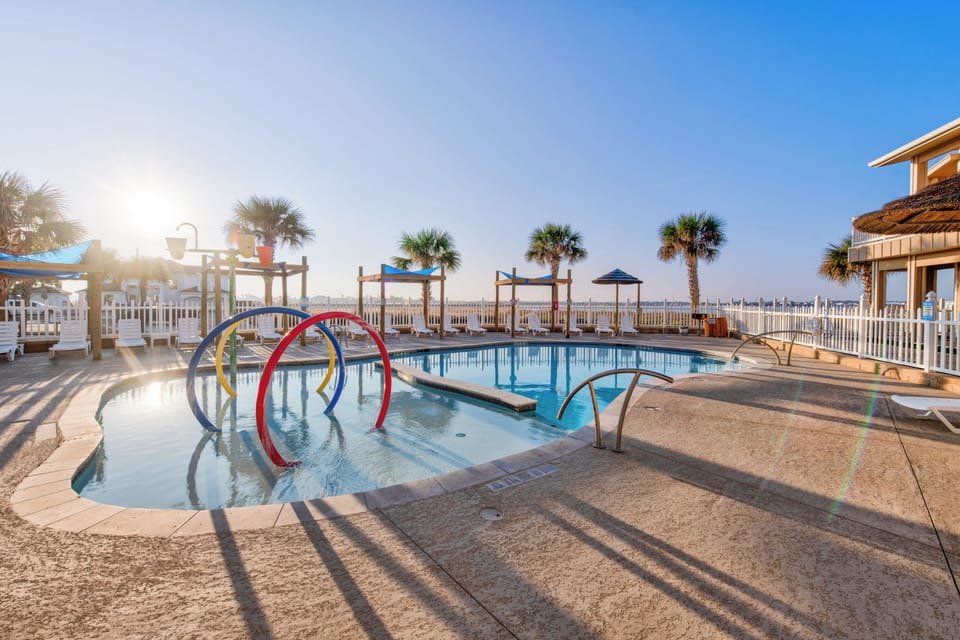 Beachfront pool area with colorful play features and palm trees, offering direct access to sandy shores and coastal recreation.