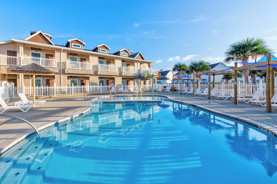 Beachfront vacation rental property featuring multiple units with private balconies surrounding a sparkling swimming pool area with tropical palm trees.