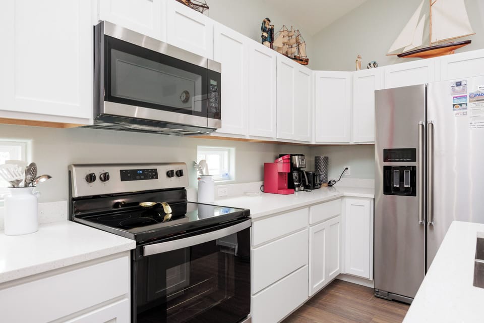 Your fully-equipped kitchen awaits with modern stainless steel appliances, crisp white cabinets, and thoughtful touches like the cheerful red coffee maker ready for your morning brew.