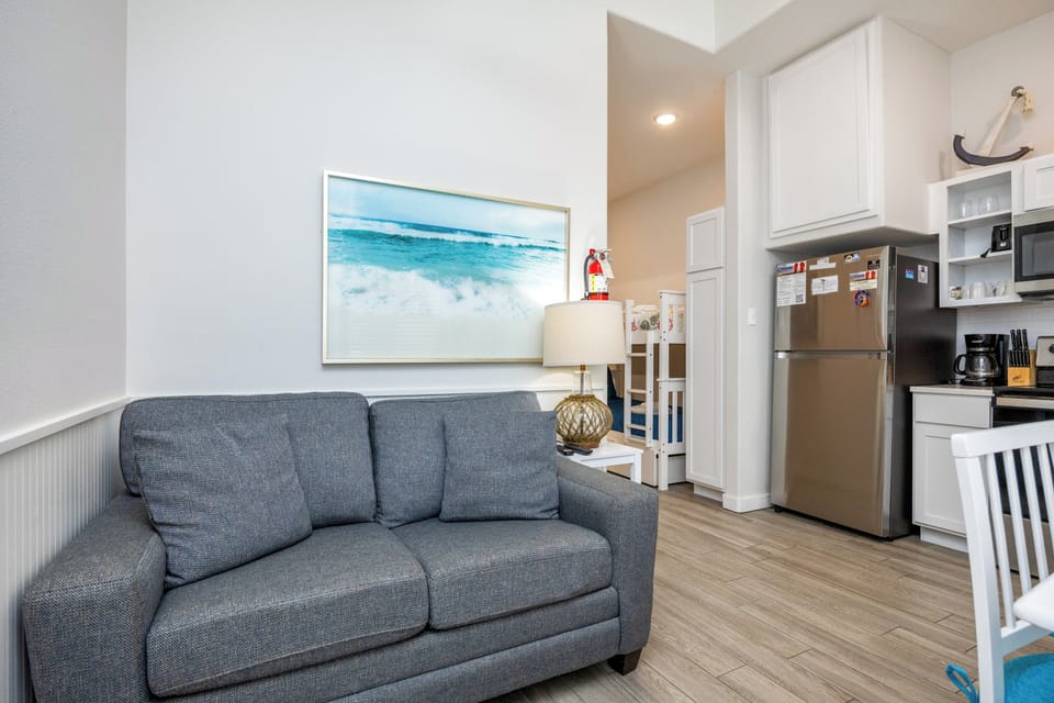 Relax on your comfortable sofa while admiring beach artwork in this bright, open living space with a fully equipped kitchen nearby.