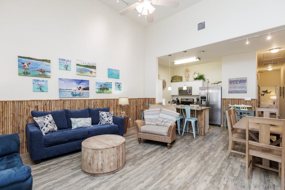 Relax in your coastal-themed living space with ocean artwork, comfy seating, and an open kitchen perfect for beach getaway meals.