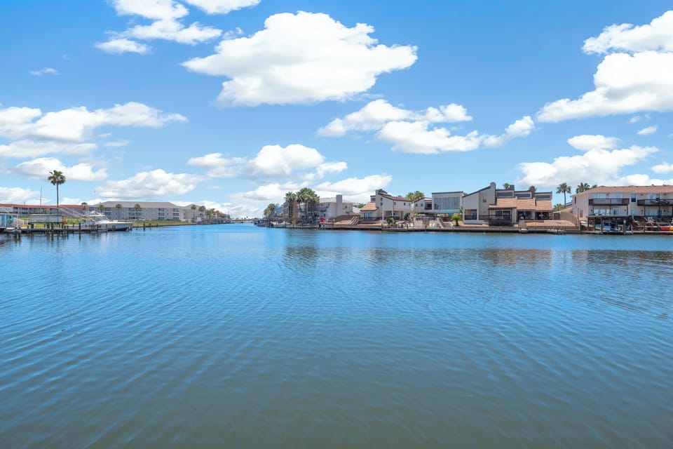A tranquil waterfront neighborhood with canal-side homes, palm trees dotting the shoreline, and serene water views under blue skies—the perfect setting for a peaceful getaway.
