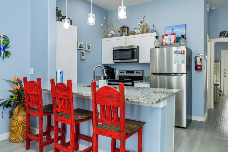 Your fully equipped kitchen awaits with stainless steel appliances, granite countertops, and cheerful red bar stools perfect for morning coffee or casual meals.