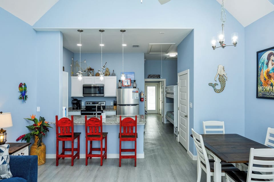 Your coastal-themed open living space features a bright kitchen with granite countertops, vibrant red bar stools, and nautical decor.