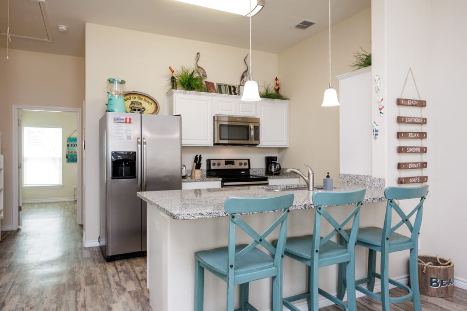 Your fully equipped kitchen features granite counters, stainless appliances, and coastal-themed seating perfect for morning coffee or casual meals.