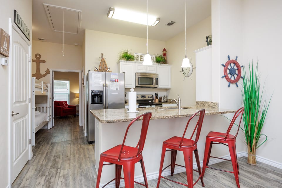 Your fully equipped kitchen features granite counters and cheerful red stools where you can enjoy morning coffee or plan your beach adventures.