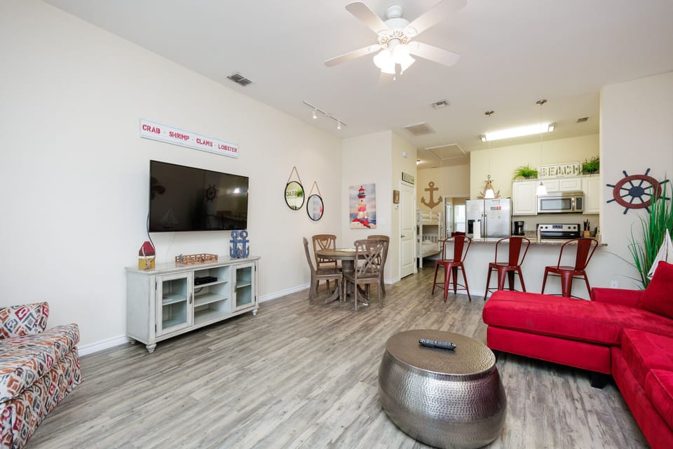 Your open-plan living space blends comfort and coastal charm, featuring a bright red sectional, entertainment center, and nautical touches throughout.