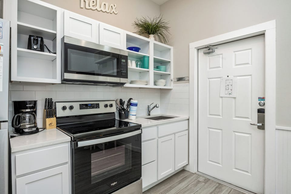 Your fully equipped kitchen awaits with crisp white cabinets, modern appliances, and thoughtful touches like the cheerful 'relax' sign—perfect for brewing morning coffee.