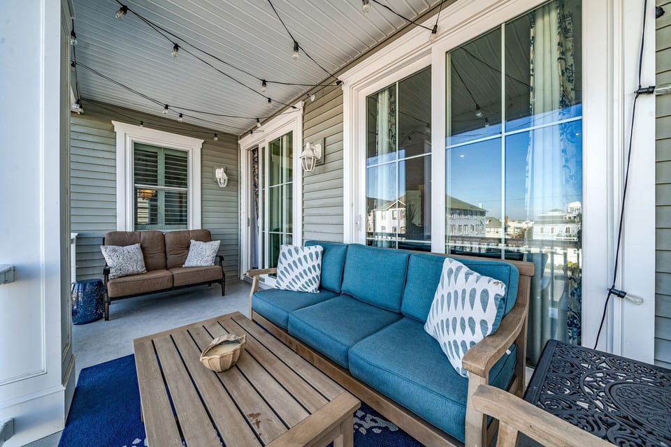 Coastal chic covered balcony with comfy seating and twinkle lights!