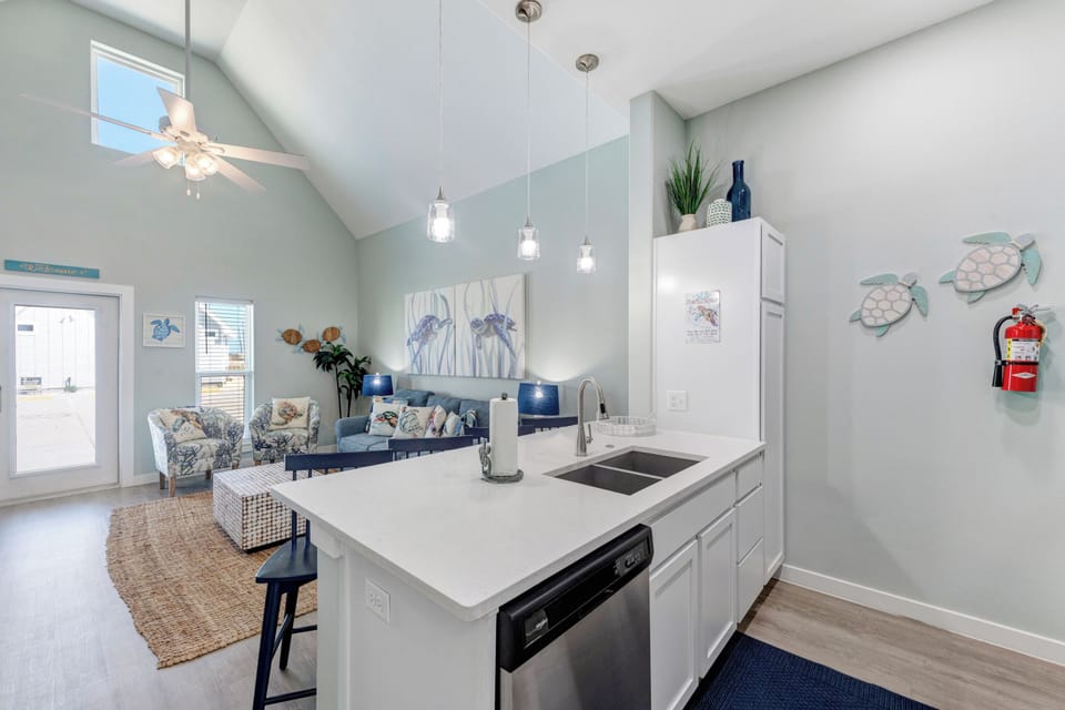 Your bright, open kitchen flows seamlessly into the coastal-themed living space, featuring modern appliances and charming sea turtle wall art.