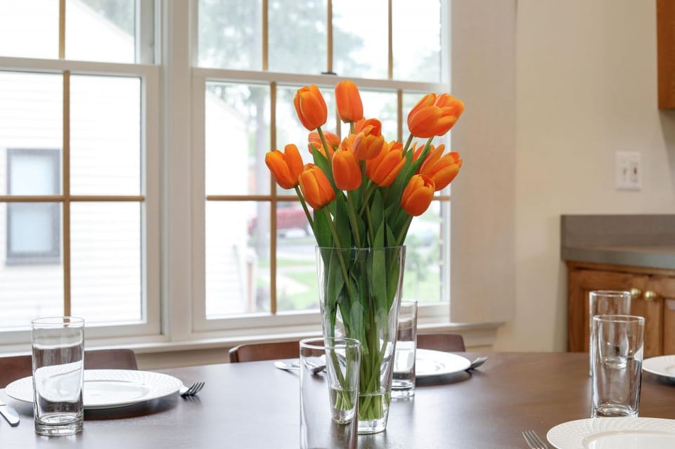 Feast your eyes on our dining table, prepped for your next homemade meal with loved ones! Dazzling tulips, sparkling glassware, gleaming silverware, and pristine plates are all set against a backdrop of warmth and charm.