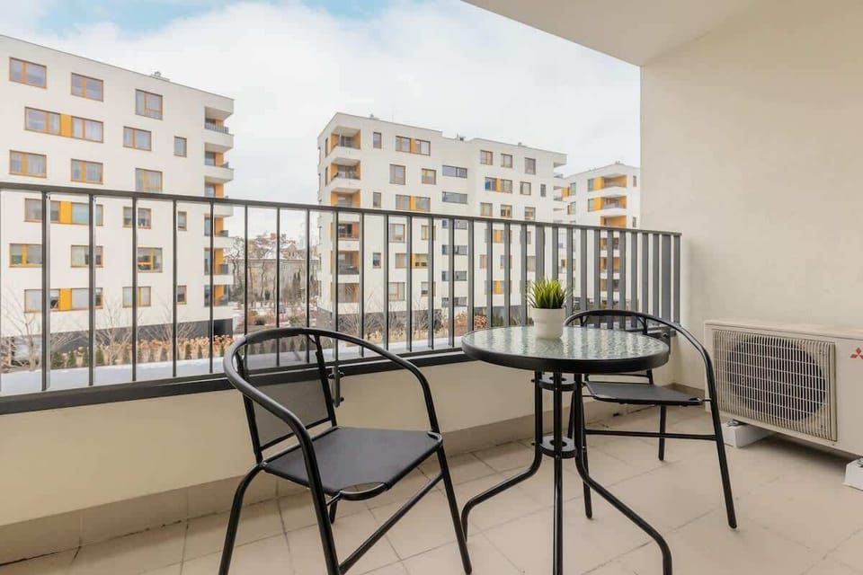 A balcony with outdoor seating, including a small round table and metal chairs, perfect for enjoying the view of the residential complex.

