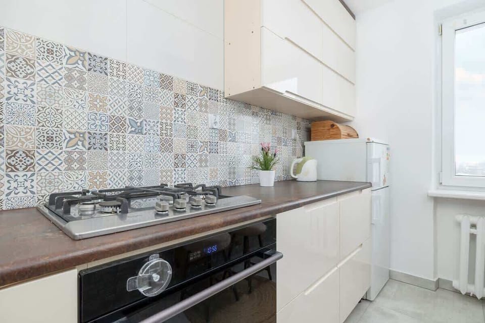 A modern kitchen with a mosaic tile backsplash, white cabinets, and stainless steel appliances, maintaining a chic and functional design.
