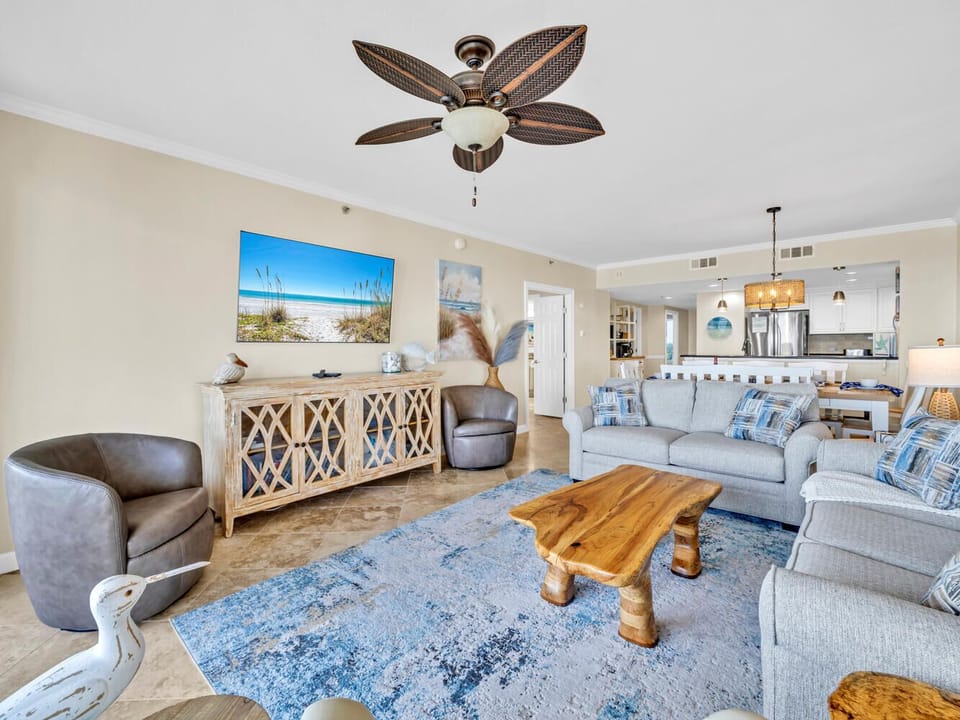 Relax in your coastal-themed living room with plush seating, tropical ceiling fan, and beach artwork creating the perfect vacation atmosphere.