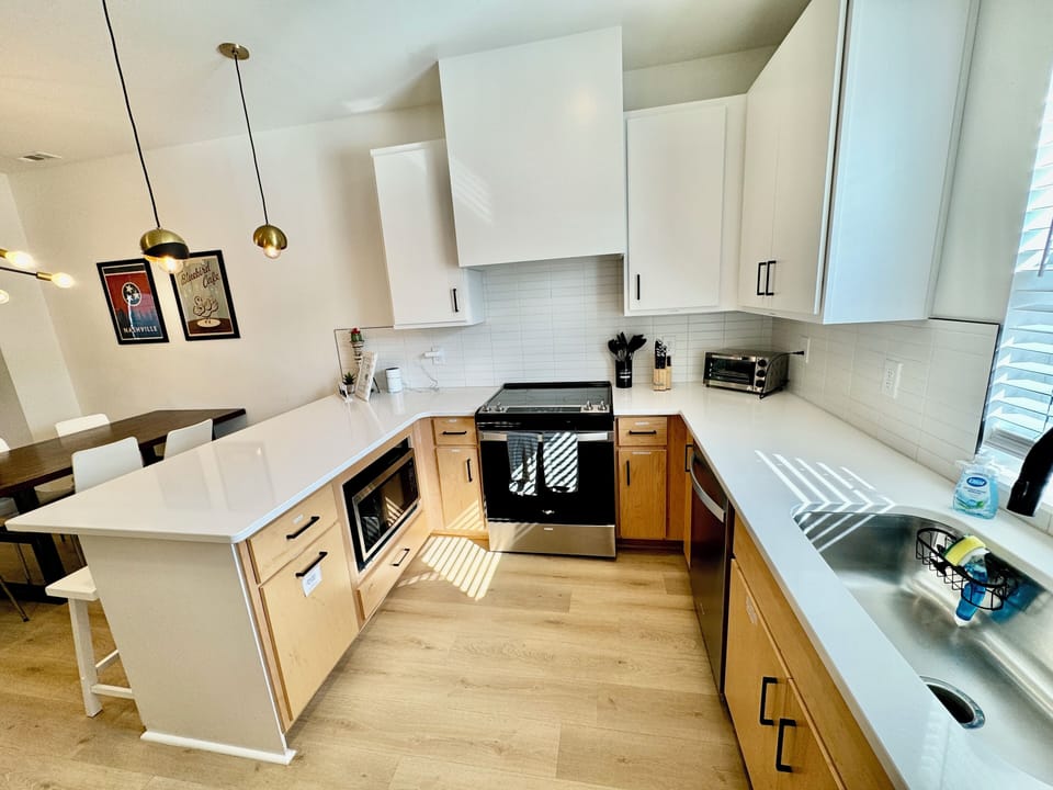 KITCHEN – This bright and modern kitchen is a chef's dream, featuring sleek stainless-steel appliances and ample countertop space. The light wood cabinets and crisp white countertops create a fresh and inviting atmosphere. Equipped with all the essentials, including a large fridge, oven, dishwasher, and small appliances like a toaster, this space makes meal prep a breeze. Penda...