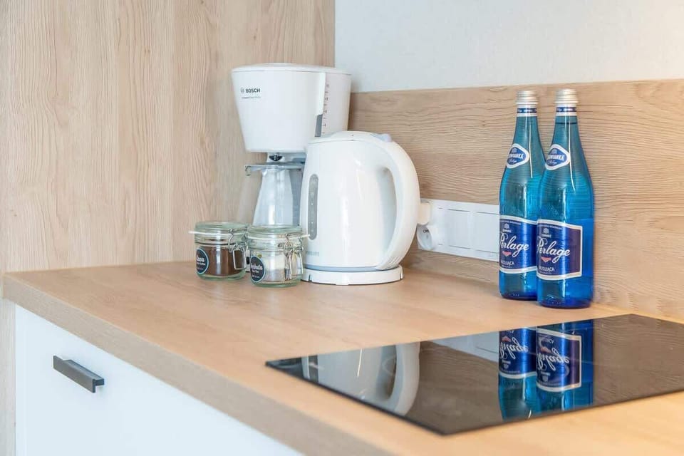 A close-up of the kitchen counter with a kettle, water bottles, and a modern induction stovetop, emphasizing functionality.
