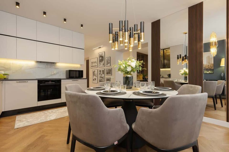 Combined living, dining, and kitchen area with white cabinets, gold details, and a cohesive design.






