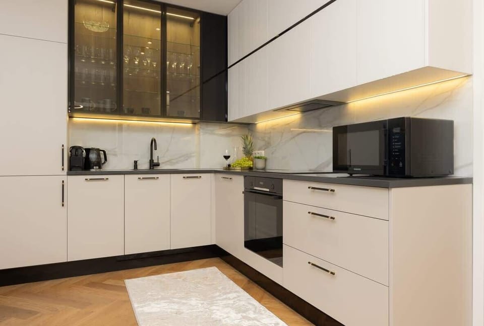Sleek kitchen with white cabinets below, black and glass cabinets above, under-cabinet lighting, and parquet flooring.
