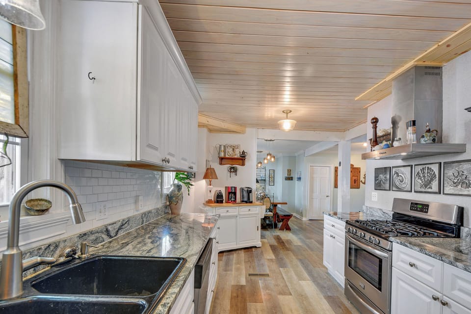 Kitchen with Granite Counters and Gas Range - Second kitchen angle shows the gas range, tile backsplash, sink, dishwasher, long counters, and open view to dining.