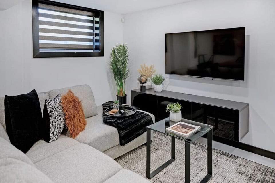 Relax in this stylish living room featuring a cozy sectional, large smart TV for entertainment, modern decor, and ample natural light. Perfect for unwinding after exploring or gathering with loved ones. Experience comfort & contemporary design!