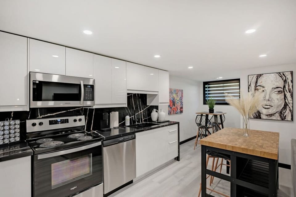 Modern full kitchen with sleek stainless steel appliances, including oven, microwave, & fridge. Features ample counter space & stylish cabinetry. Adjacent island with seating and artwork for a vibrant feel. Perfect for home-cooked meals during your stay.