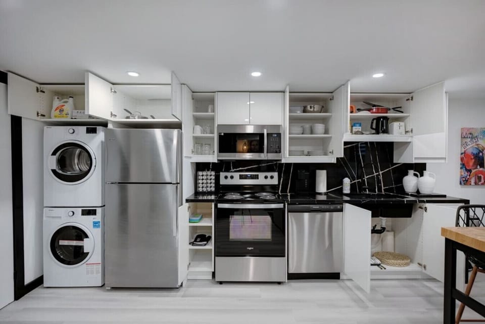 Fully equipped kitchen with stainless steel appliances including a fridge, oven, and microwave. Features a stacked washer/dryer for convenience. Ample white cabinetry & counter space for all your cooking needs. Perfect for extended stays!