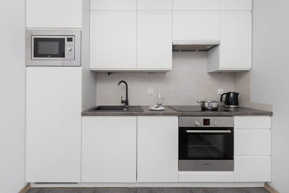 Compact kitchen with white cabinets, built-in oven, and a microwave.

