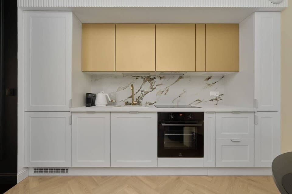Kitchen with white cabinets, gold accents, and marble backsplash.
