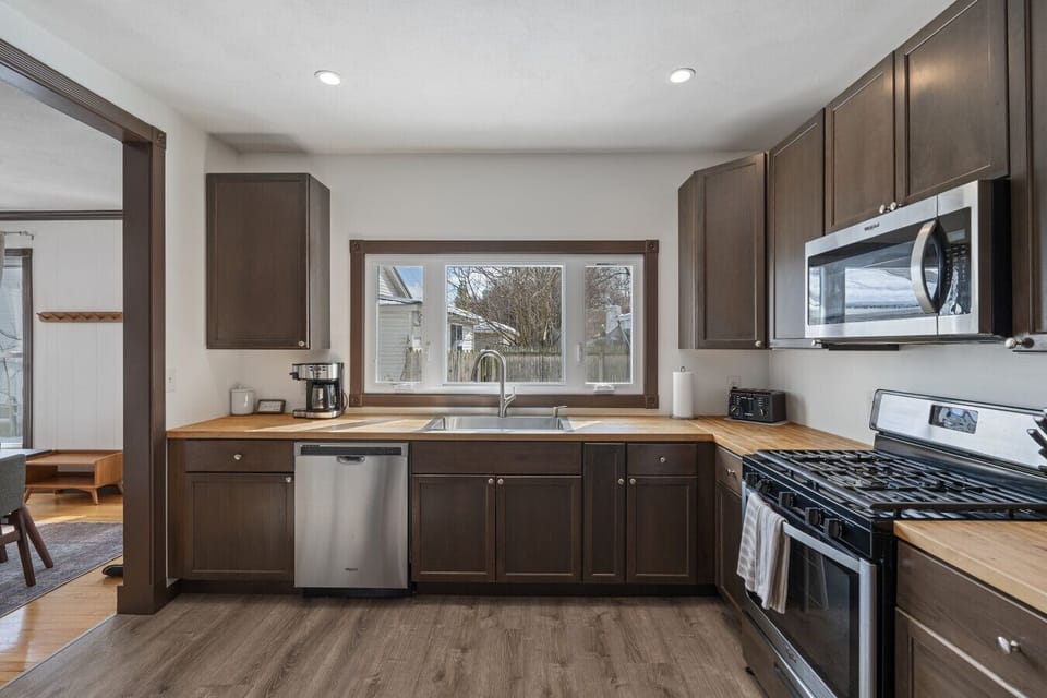 The fully equipped kitchen offers a gas stove, microwave, dishwasher, and large sink with a butcher block countertop for prepping meals. Natural light from the window keeps the space bright and inviting. Ideal for everything from a quick coffee to gourmet