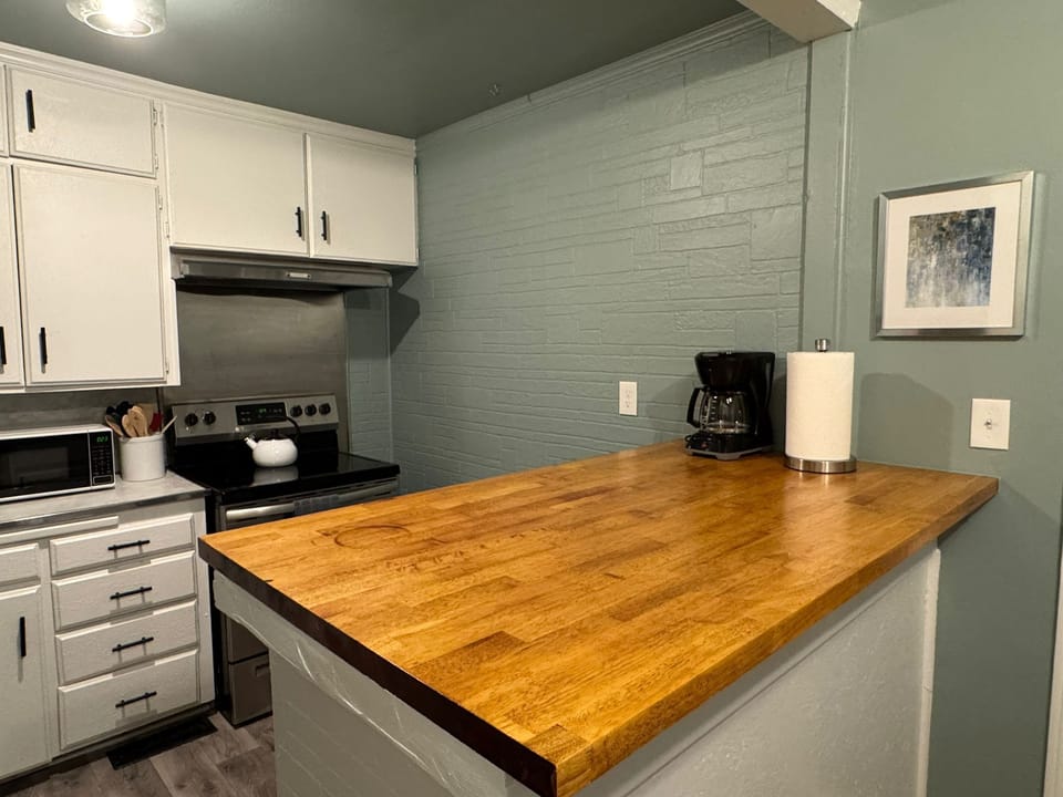 Compact kitchen with full stove, coffee maker, and prep-ready butcher-block counter.