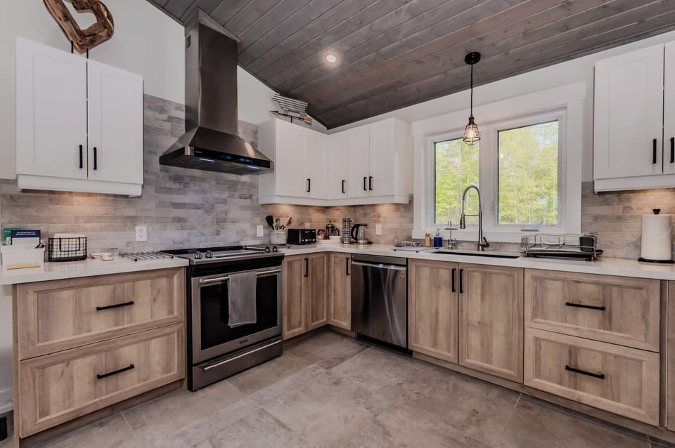 Sleek counters, a range hood, and bright natural lighting. The combination of white and wood cabinetry along with a neutral-toned backsplash creates a stylish and functional cooking area.