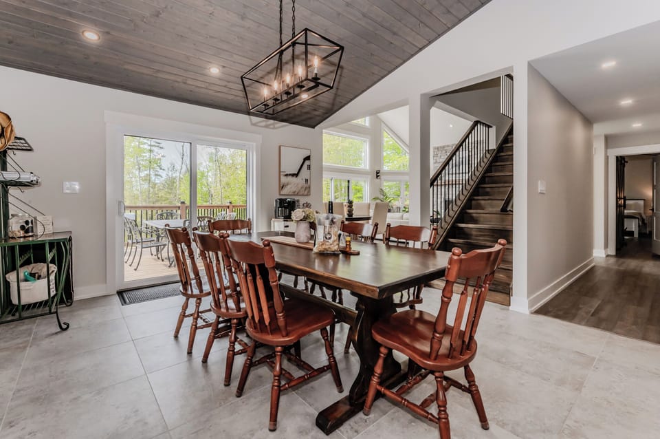 The dining area, with its rustic wooden table and chairs, exudes a warm, welcoming vibe. Overhead, a modern chandelier adds a touch of elegance, while the open layout connects seamlessly to the living room and kitchen.